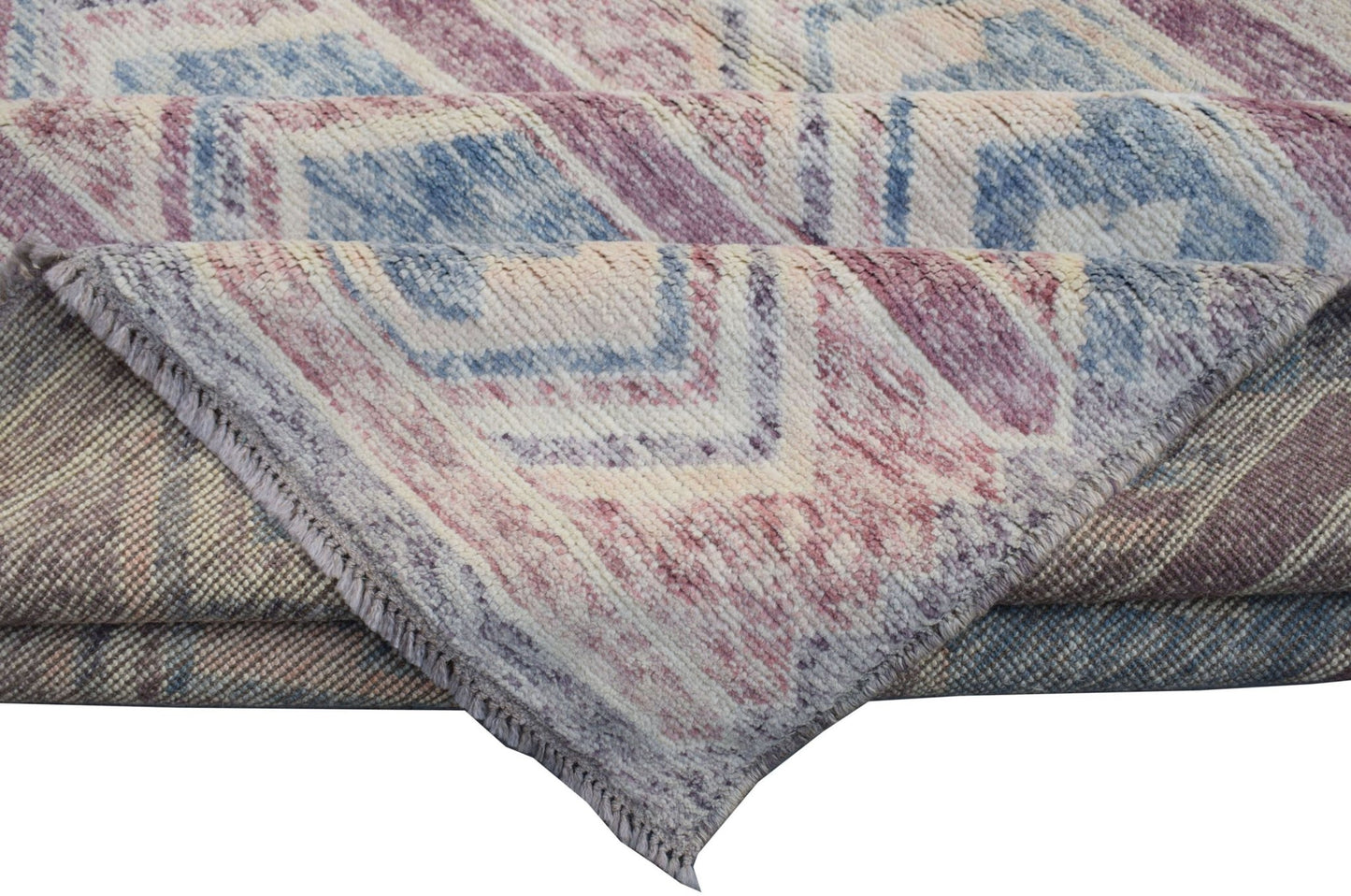 A folded Afghan Pashm wool rug featuring a geometric pattern in shades of blue, pink, and cream.