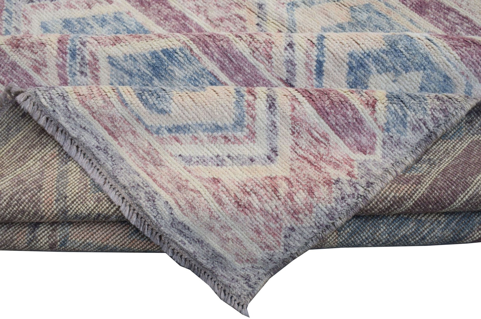 A folded Afghan Pashm wool rug featuring a geometric pattern in shades of blue, pink, and cream.
