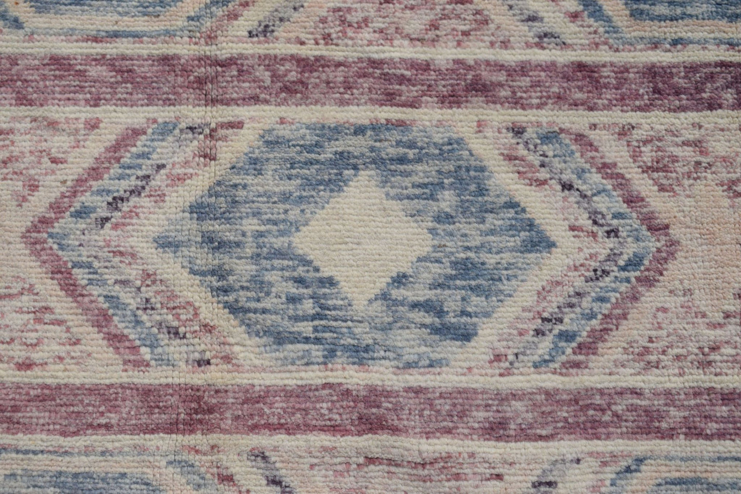 A handmade Afghan wool rug featuring a geometric diamond pattern in shades of blue and mauve.