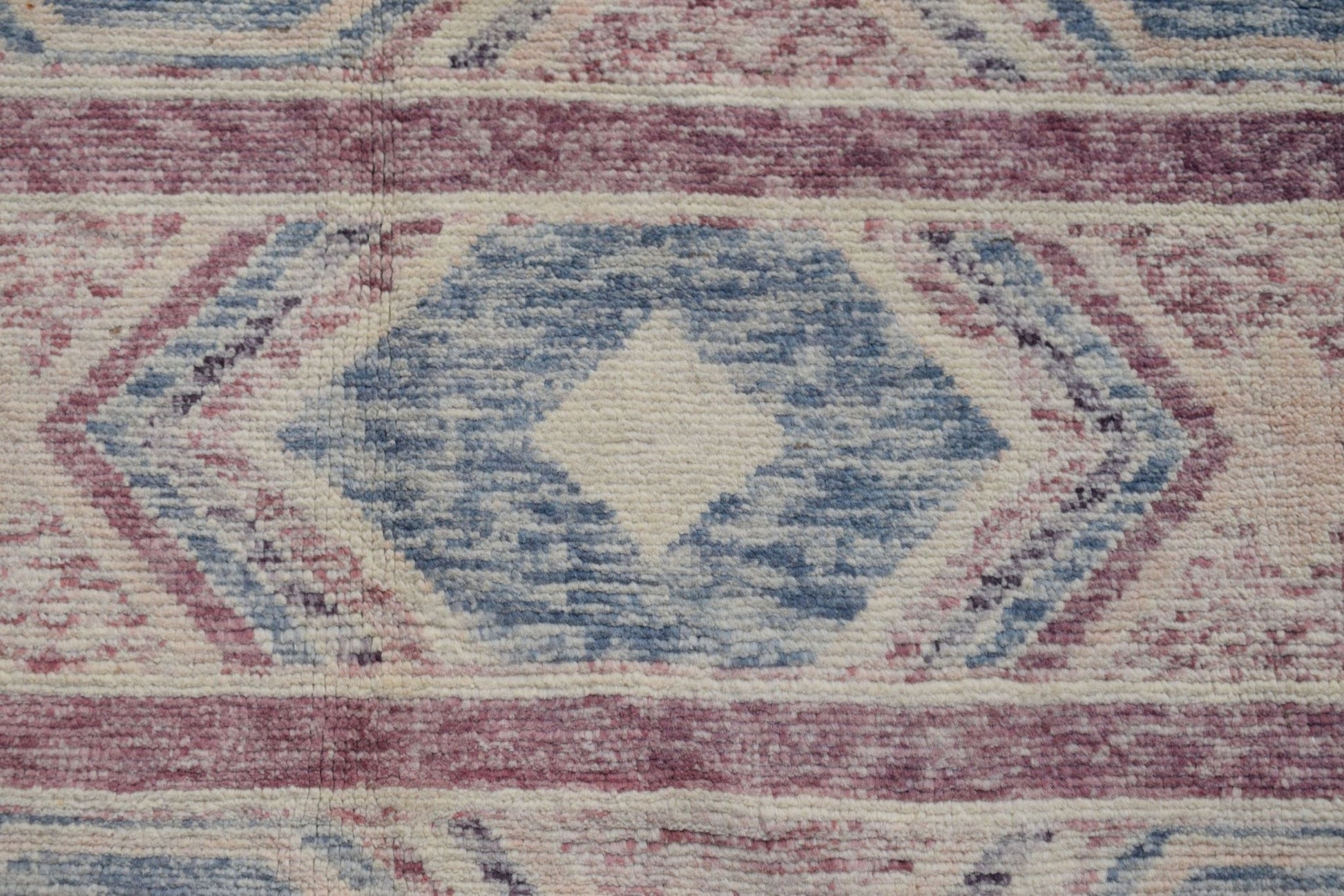 A handmade Afghan wool rug featuring a geometric diamond pattern in shades of blue and mauve.