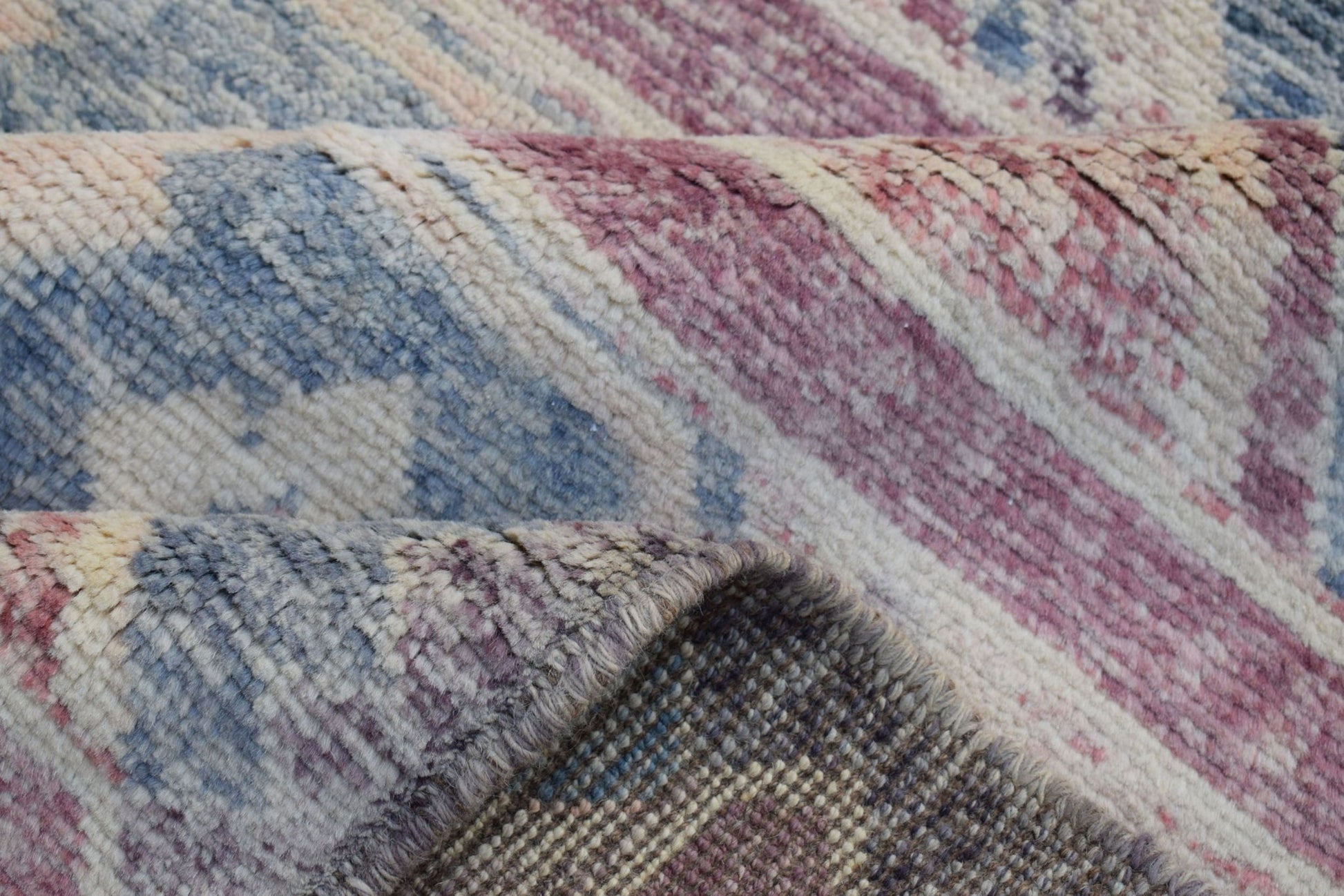 A close-up view of a handmade Afghan wool rug featuring a folded corner with blue and pink patterns.