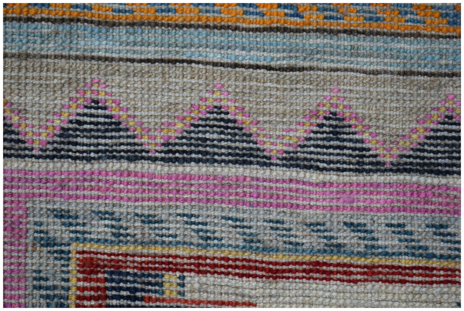 A close-up of a handmade Afghan wool rug featuring geometric patterns in pink, blue, and black.