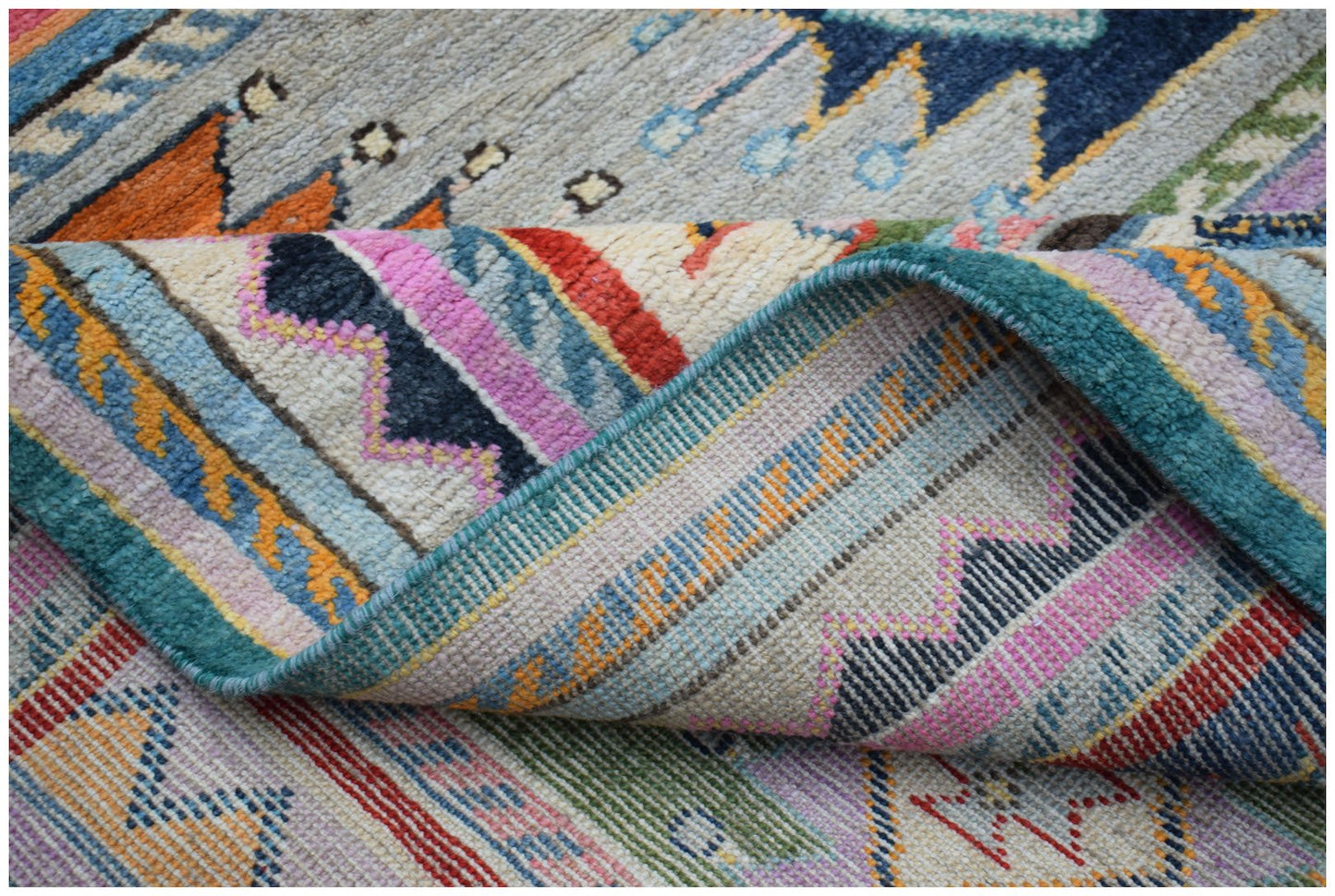 A close-up of a handmade Afghan wool rug featuring colorful geometric patterns and a folded edge.