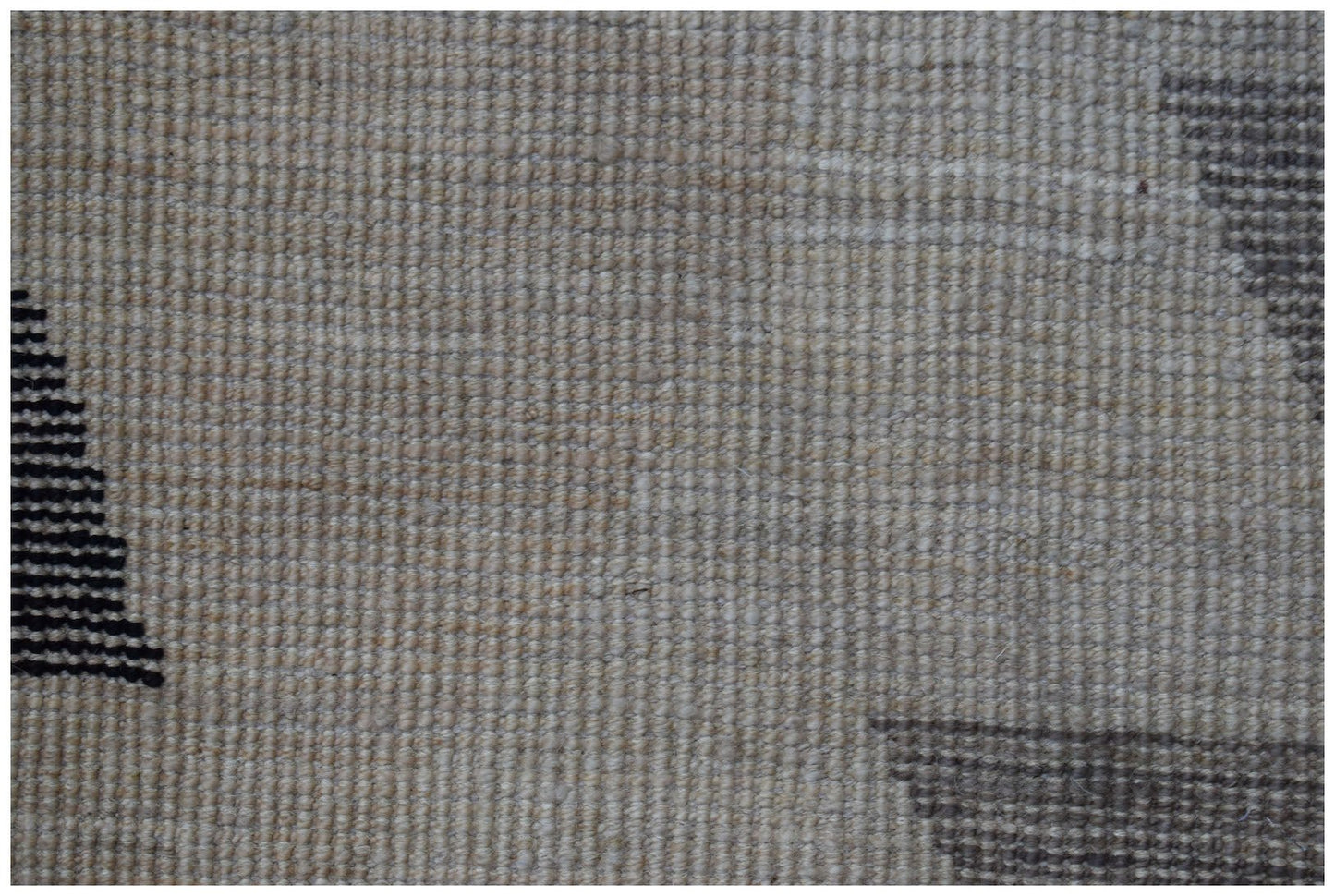 A close-up of a handmade Afghan wool rug featuring a neutral textured background with dark patterns.