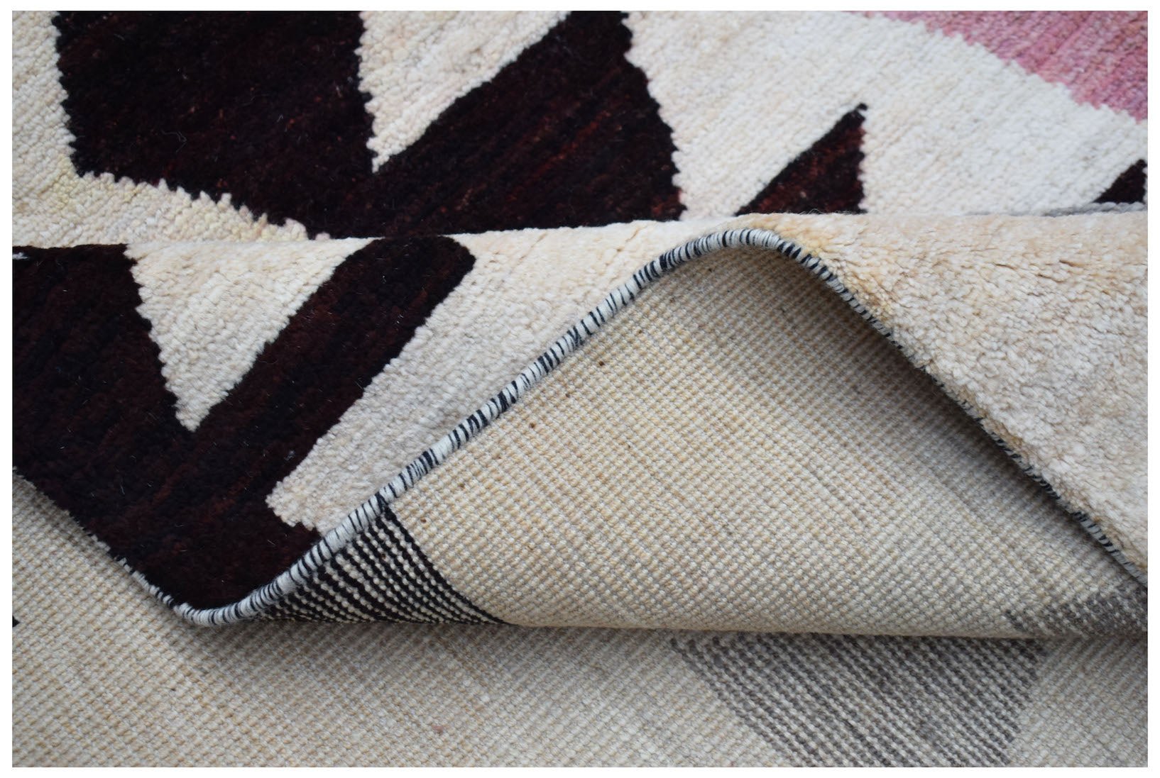 A corner of a handmade Afghan wool rug with a geometric pattern in dark brown and cream.