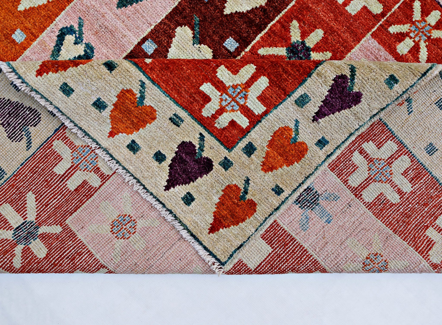 A handmade wool rug featuring a geometric pattern of floral motifs in red, orange, and cream.