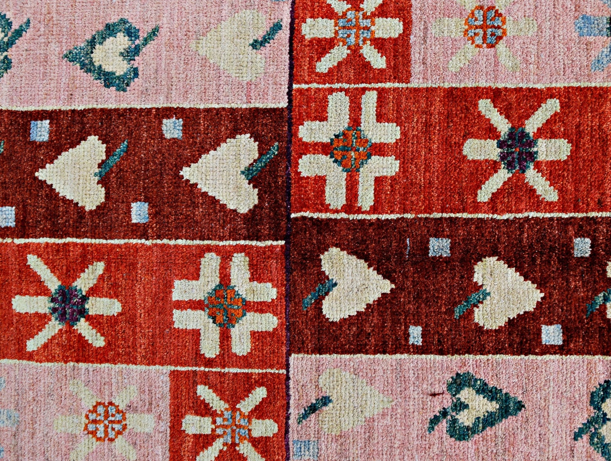 A handmade wool rug featuring a geometric patchwork pattern of floral and leaf motifs in red tones.