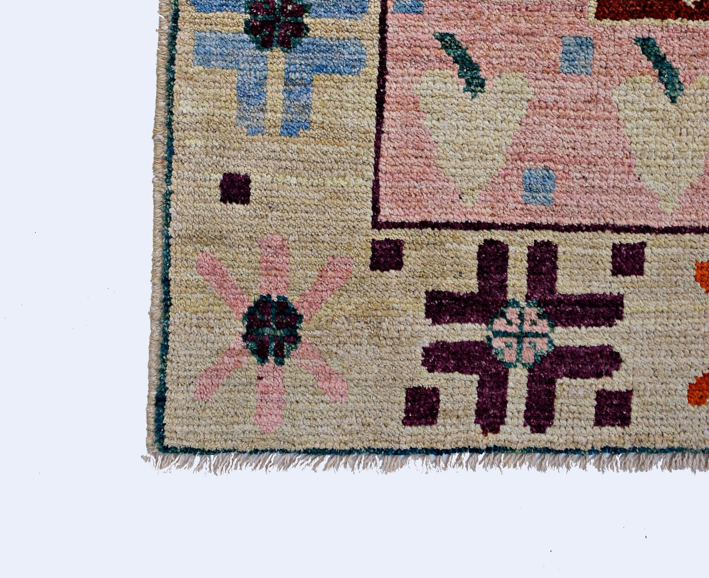 A handmade wool rug from Afghanistan featuring a geometric pattern with floral motifs in pink, blue, and dark purple on a cream background.