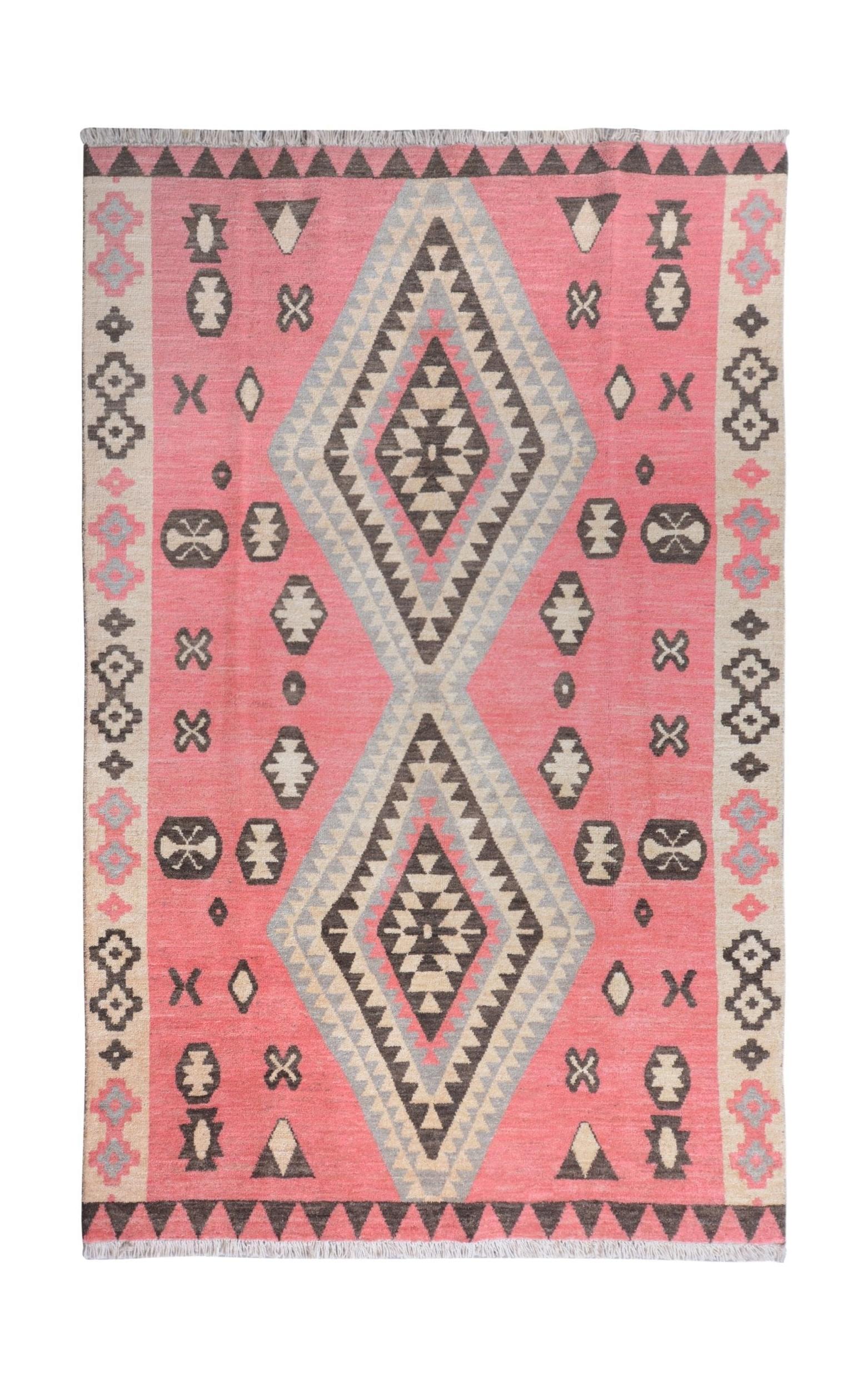 A handmade wool rug featuring a pink background with large central diamonds and tribal motifs.
