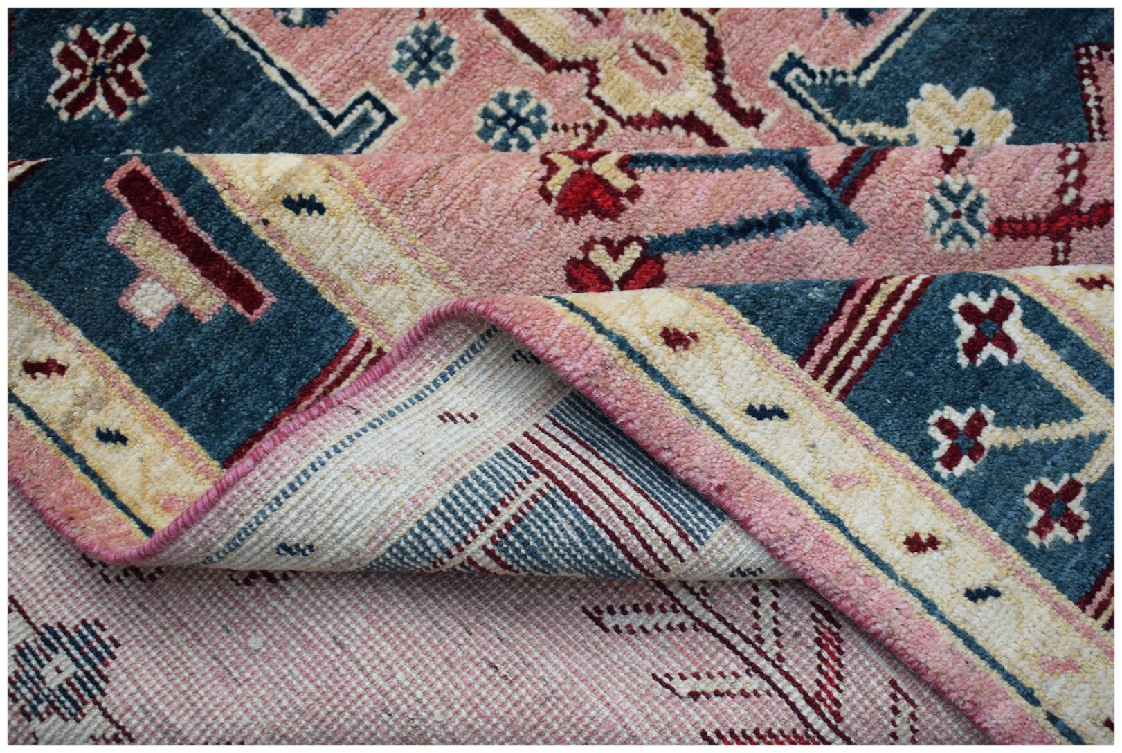 A handmade Afghan wool rug featuring a geometric floral pattern in shades of pink, blue, and cream.