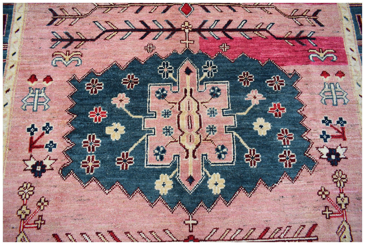 Handmade Afghan Pashm rug featuring a central blue medallion with floral motifs on a pink field.