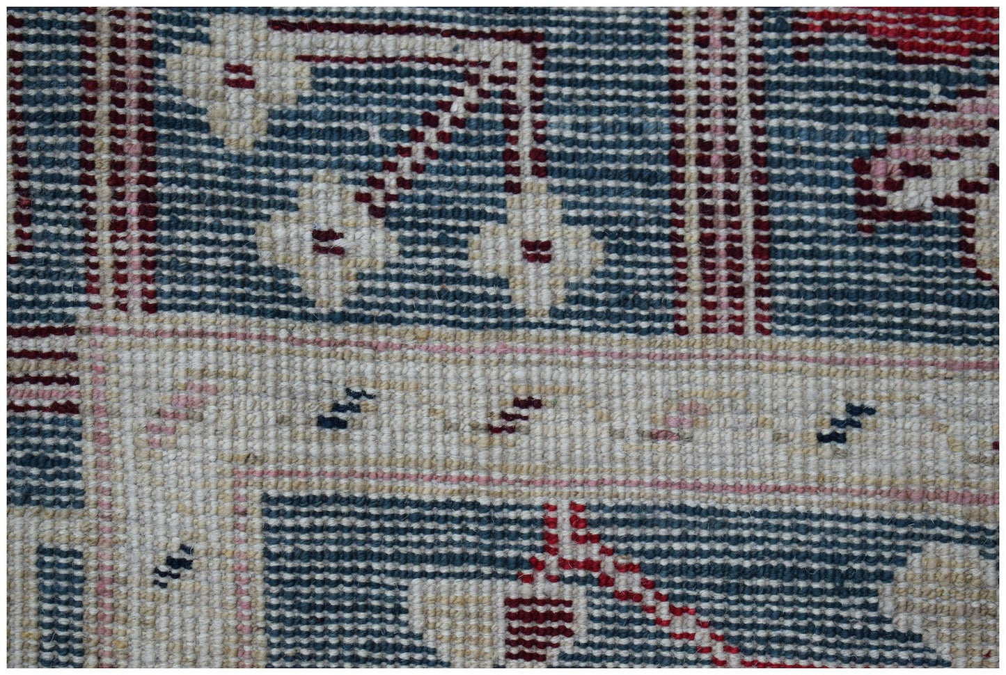 A close-up of a handmade Afghan wool rug featuring geometric floral patterns in blue and cream.