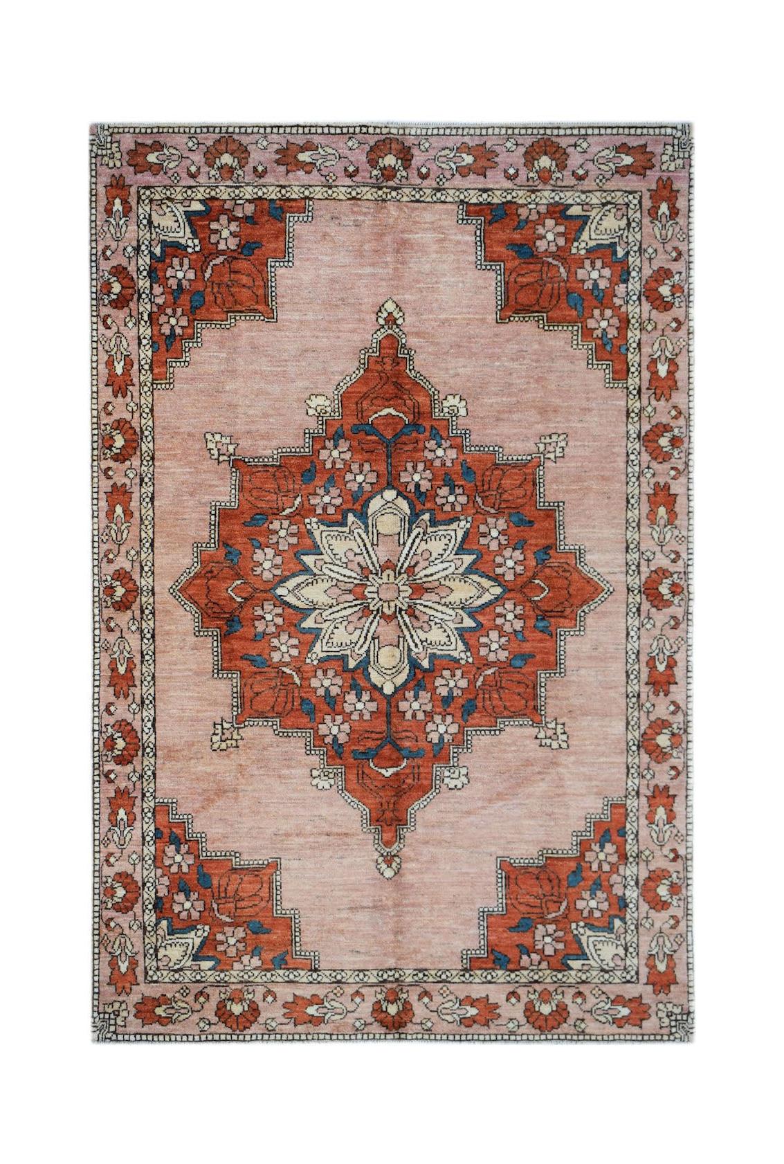 Handmade Afghan Kohi wool rug featuring a central floral medallion on a soft pink background.