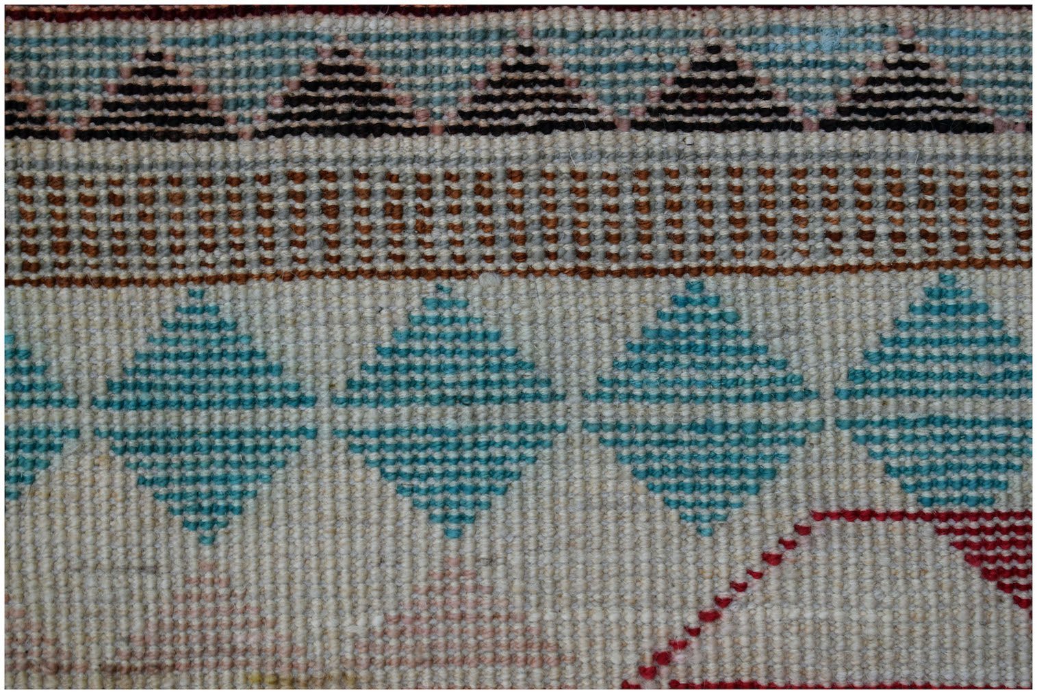 A close-up of a handmade Afghan wool rug featuring geometric patterns in blue, brown, and red.