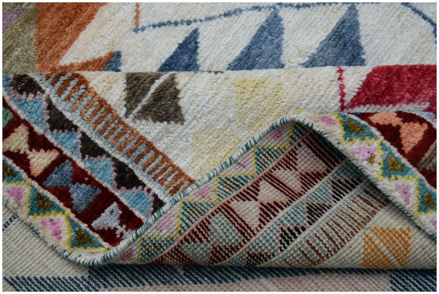A handmade Afghan wool rug featuring a colorful geometric tribal pattern with a folded corner.