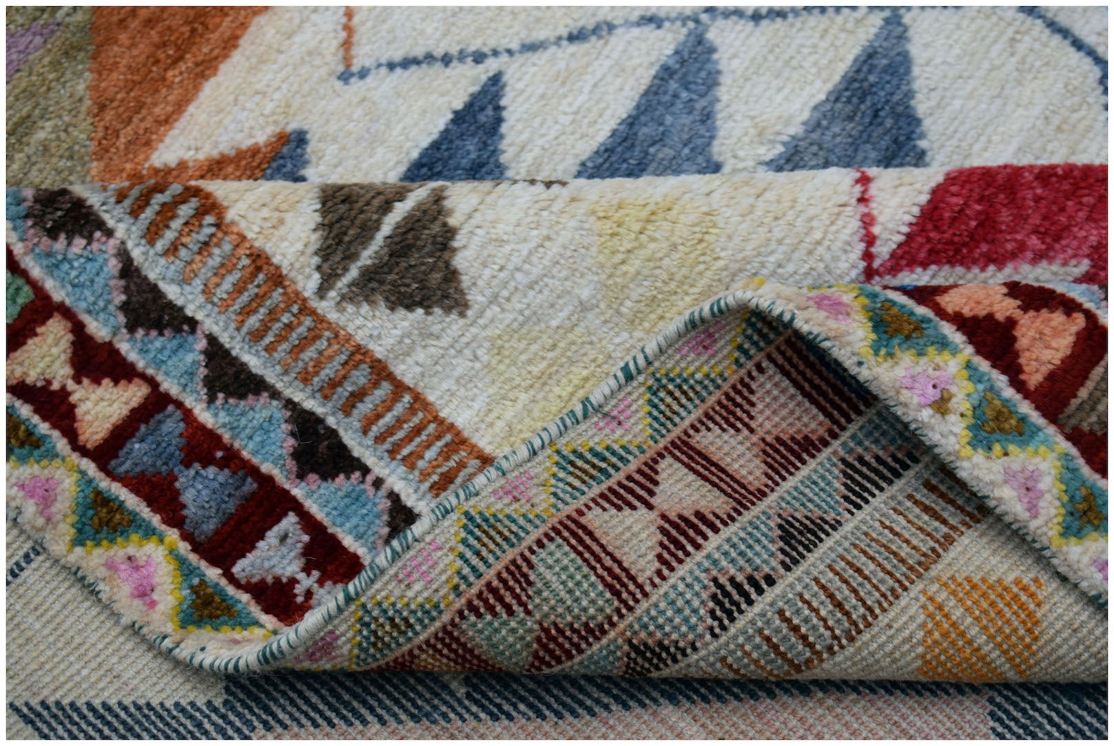 A handmade Afghan wool rug featuring a colorful geometric tribal pattern with a folded corner.