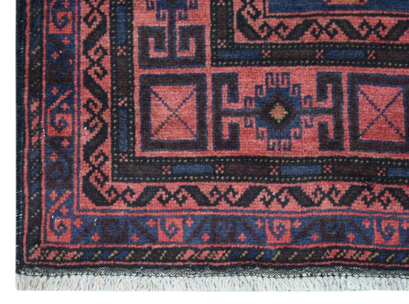A vintage handmade Afghan Baluch rug featuring geometric patterns in red and dark blue.