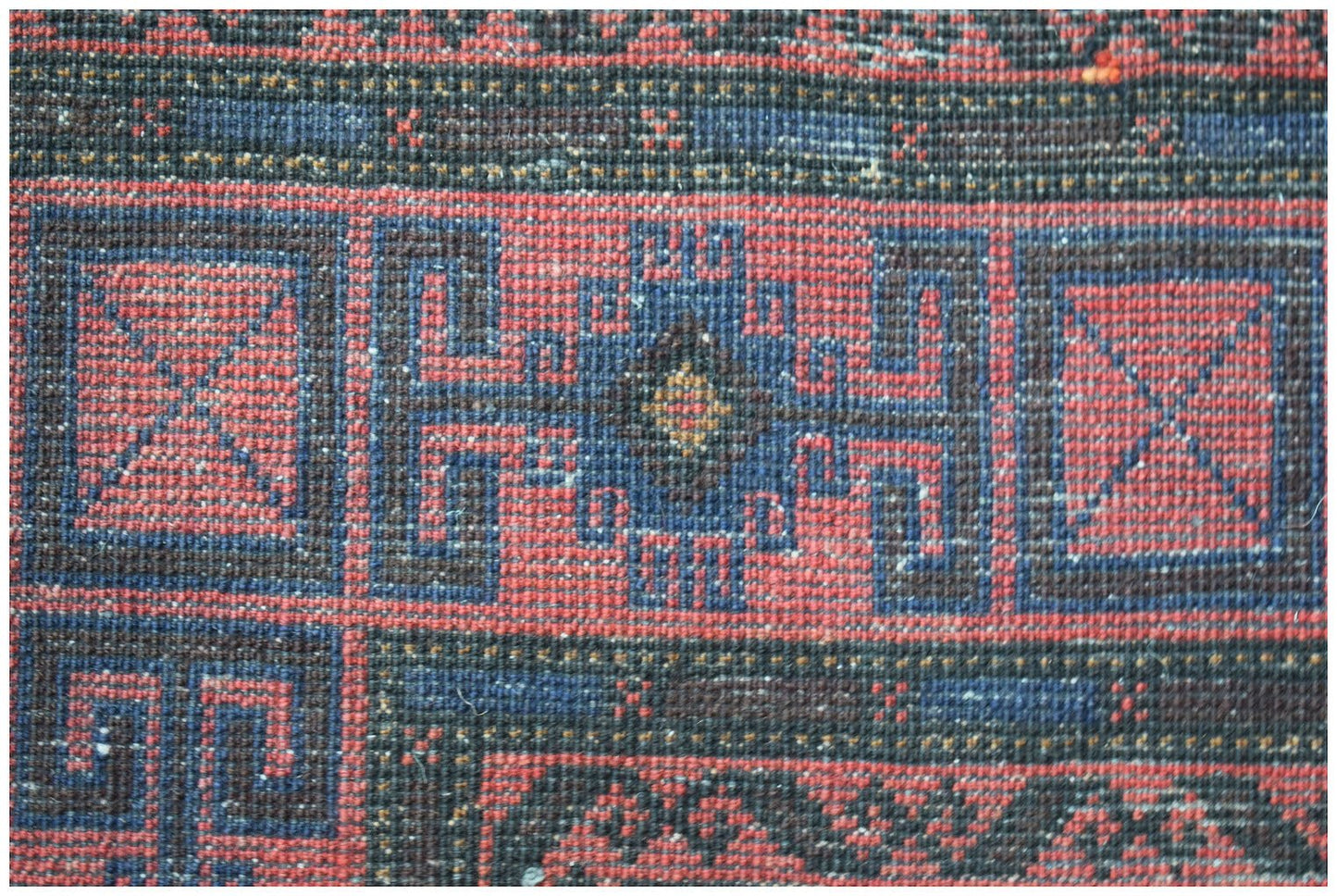 A close-up of a vintage Afghan Baluch rug featuring geometric patterns in red, blue, and black.