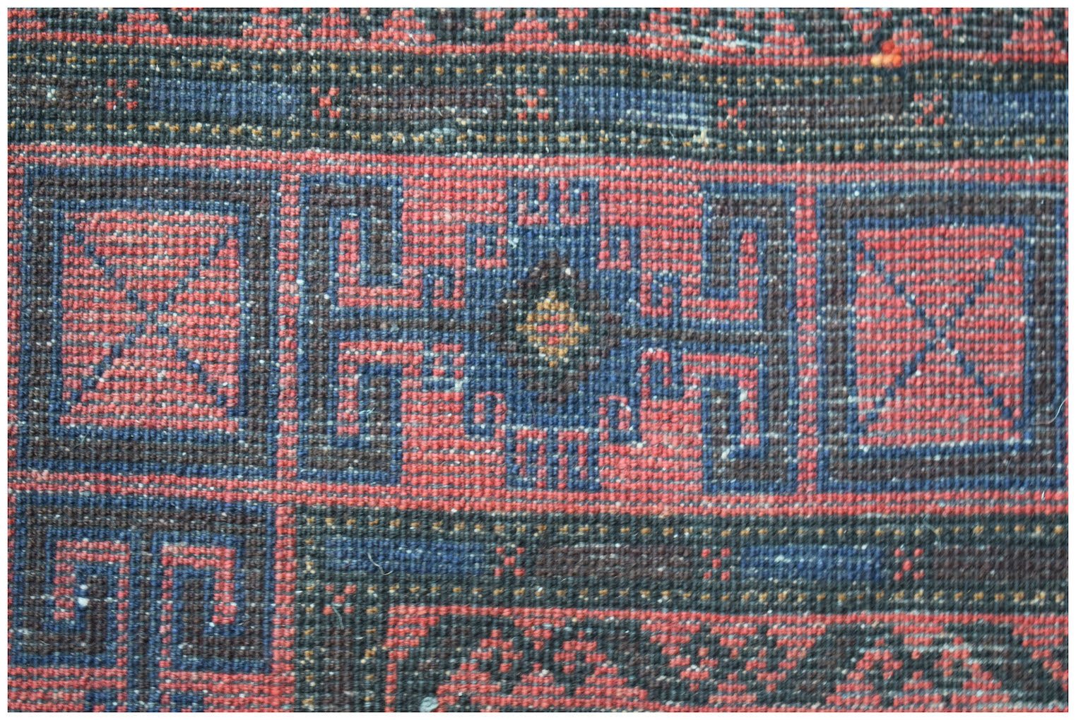 A close-up of a vintage Afghan Baluch rug featuring geometric patterns in red, blue, and black.
