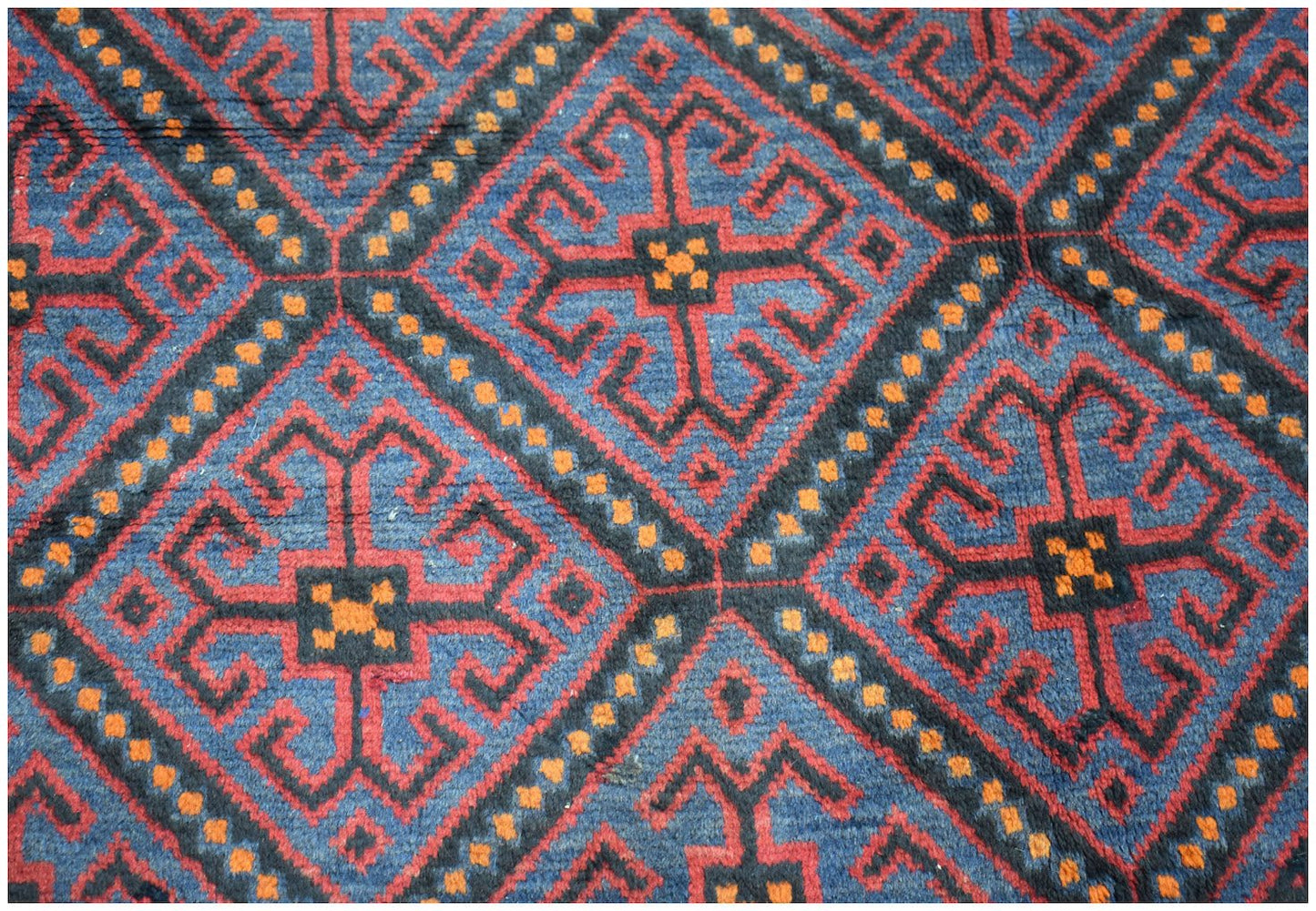 A vintage Afghan Baluch rug featuring a repeating geometric diamond pattern in blue, red, and orange.