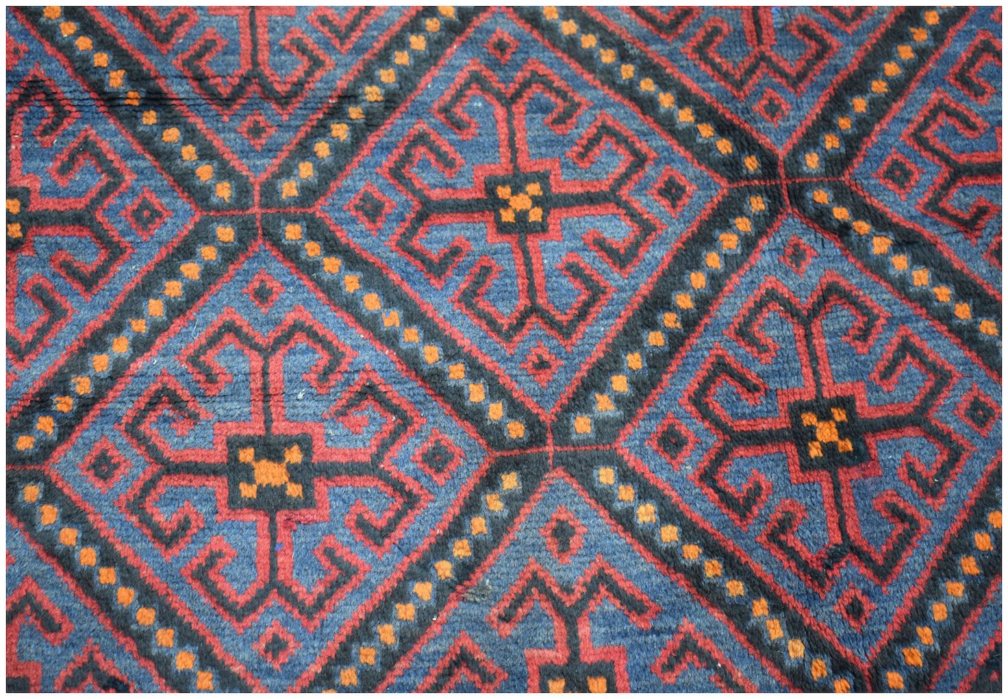 A vintage Afghan Baluch rug featuring a repeating geometric diamond pattern in blue, red, and orange.
