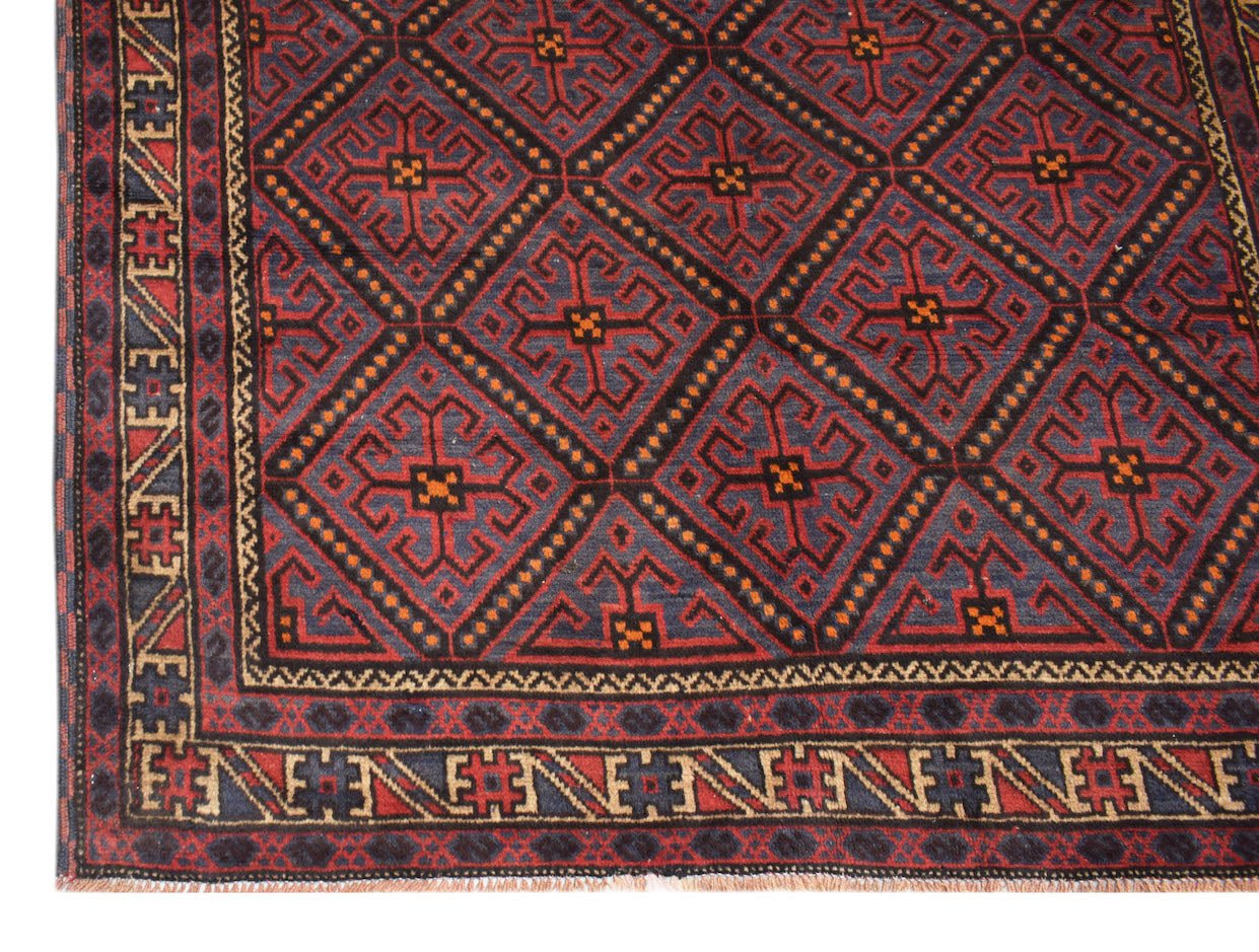 A vintage Afghan Baluch rug featuring a repeating geometric diamond pattern in red and dark blue.