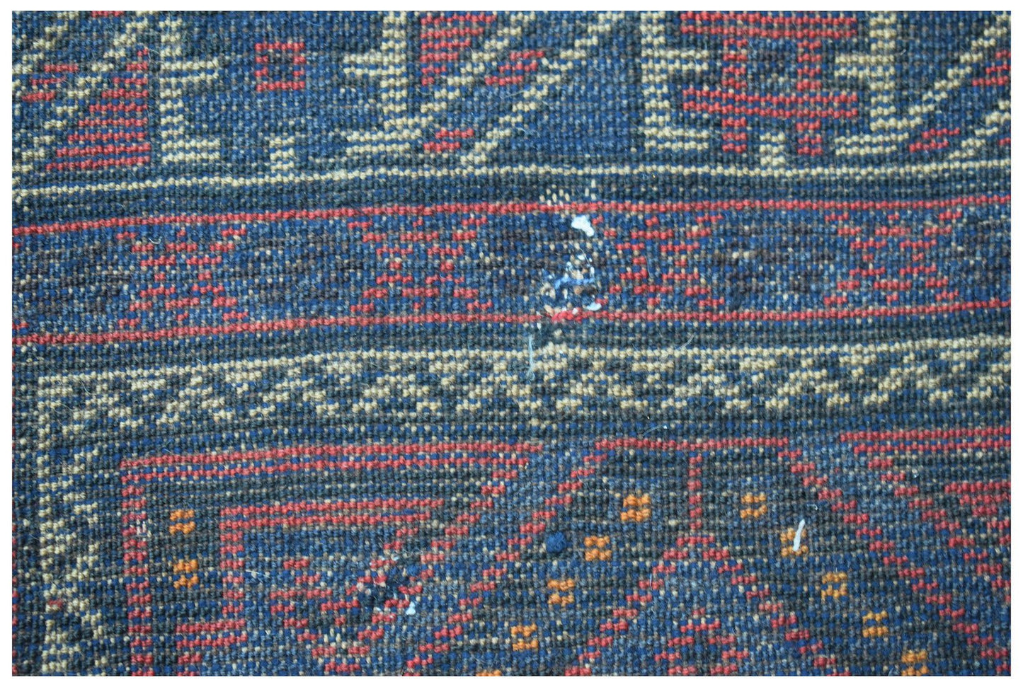A close-up of a vintage handmade Afghan Baluch wool rug featuring geometric patterns in blue and red.