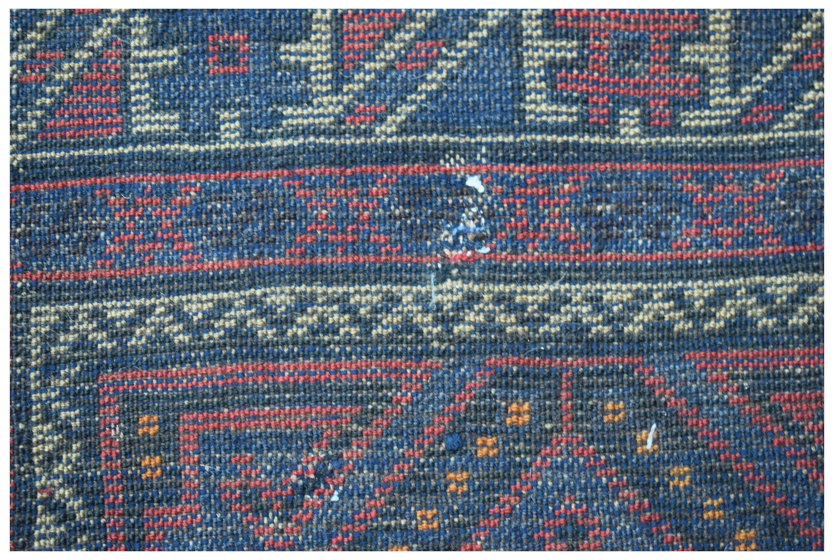 A close-up of a vintage handmade Afghan Baluch wool rug featuring geometric patterns in blue and red.