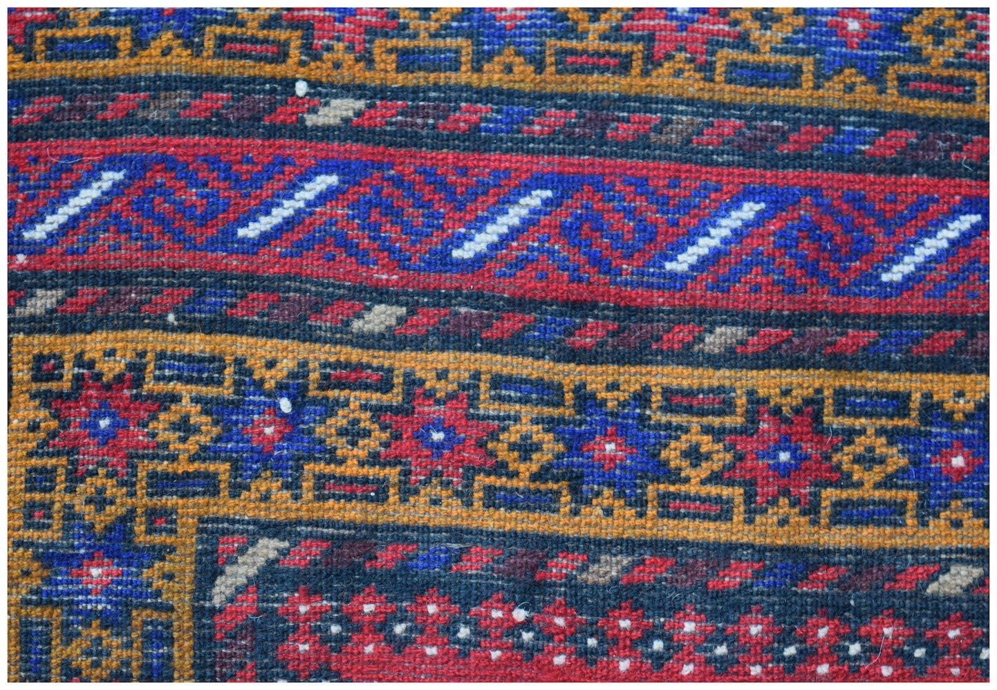 A close-up of a vintage Afghan Baluch rug featuring intricate geometric patterns in wool.