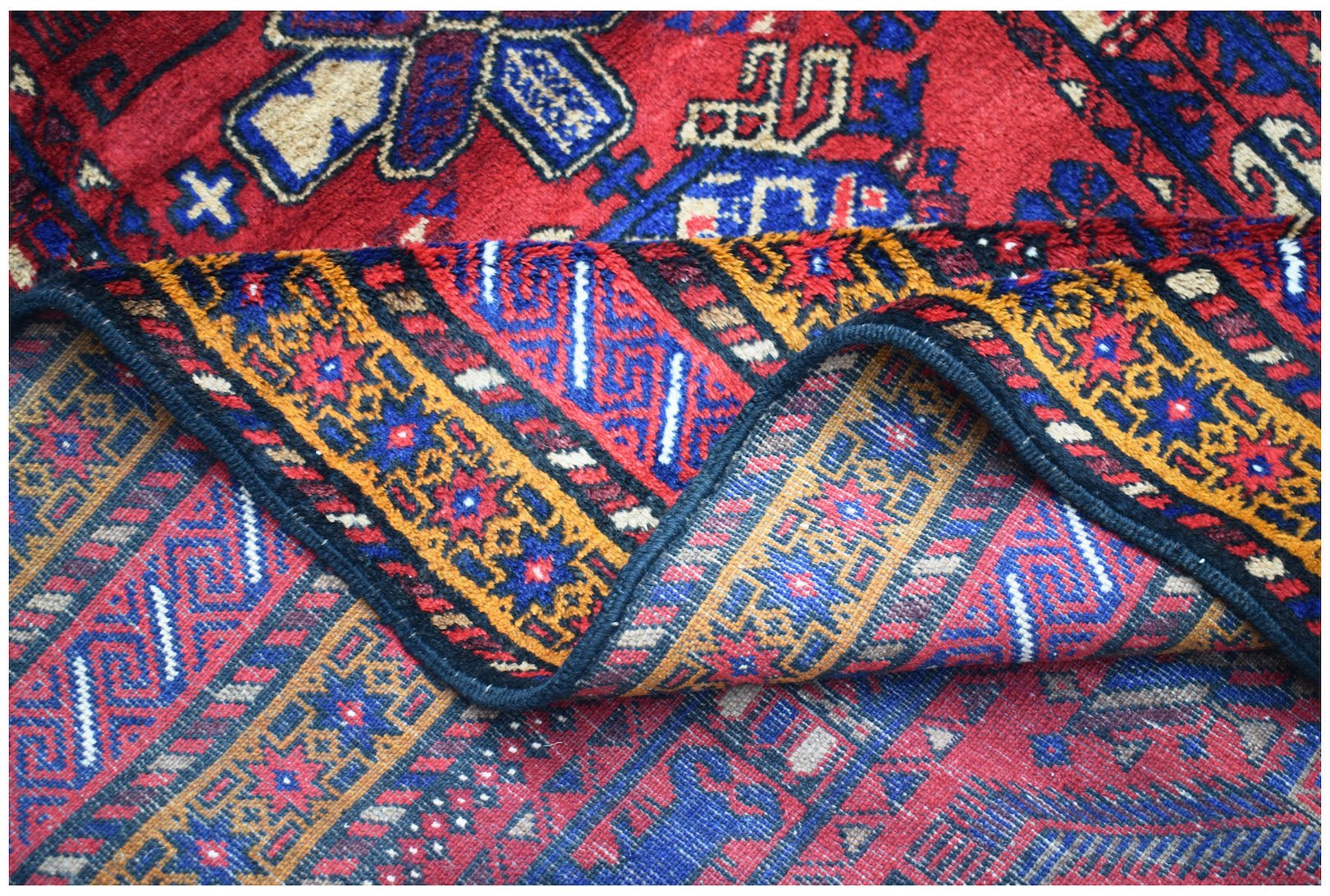 A folded vintage Afghan Baluch rug featuring intricate geometric patterns in red, blue, and gold.