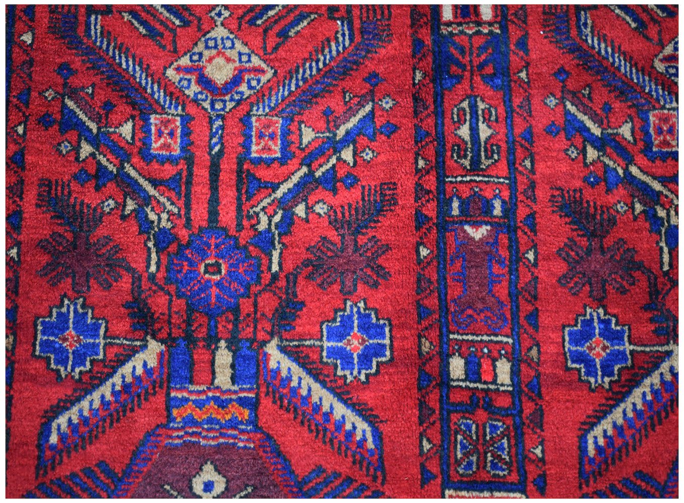 A vintage handmade Afghan Baluch wool rug featuring intricate geometric patterns in red and blue.