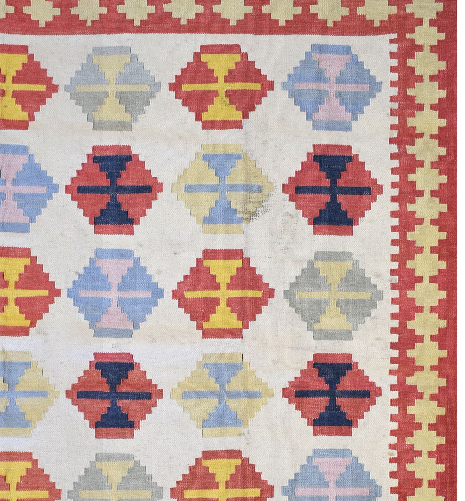 Handmade Turkish wool and cotton kilim rug featuring a repeating geometric pattern in red and blue.