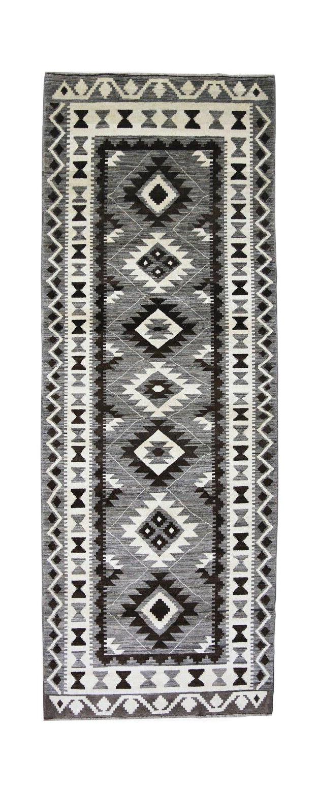 A handmade Afghan runner rug featuring a geometric diamond pattern in shades of grey and white.