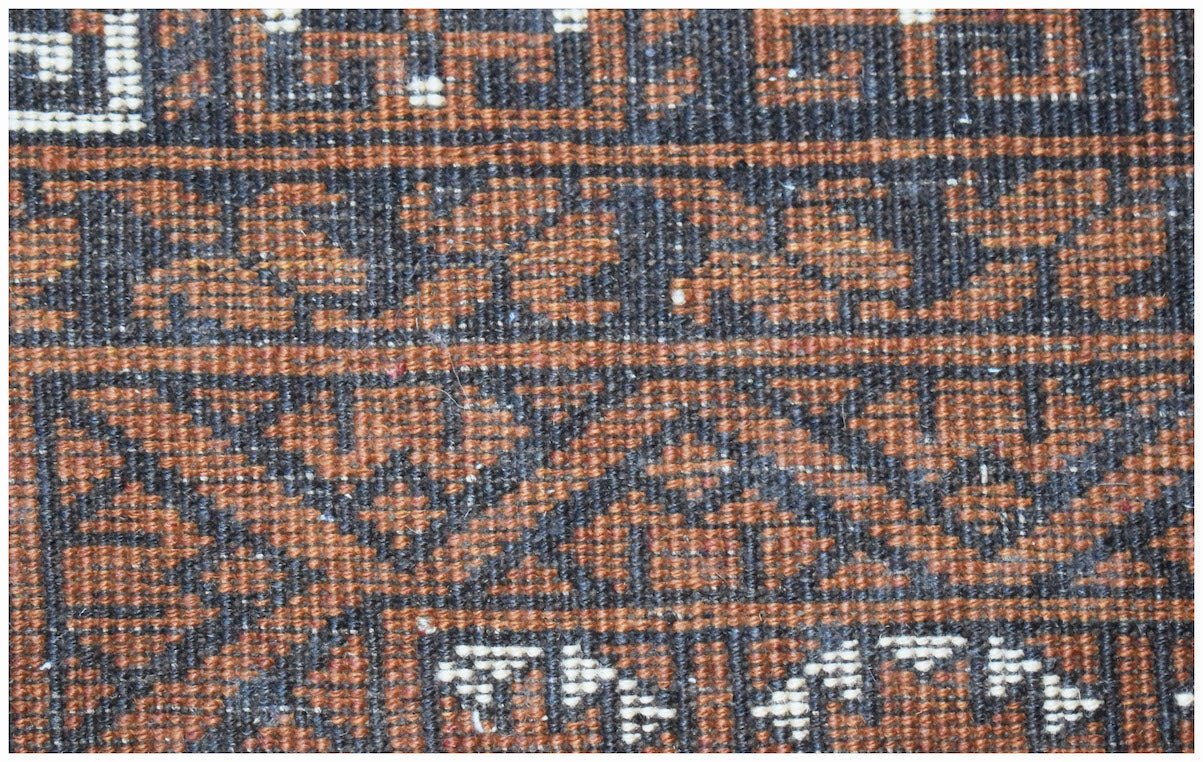 A close-up of a vintage Afghan Turkmen rug featuring intricate geometric patterns in brown and black.