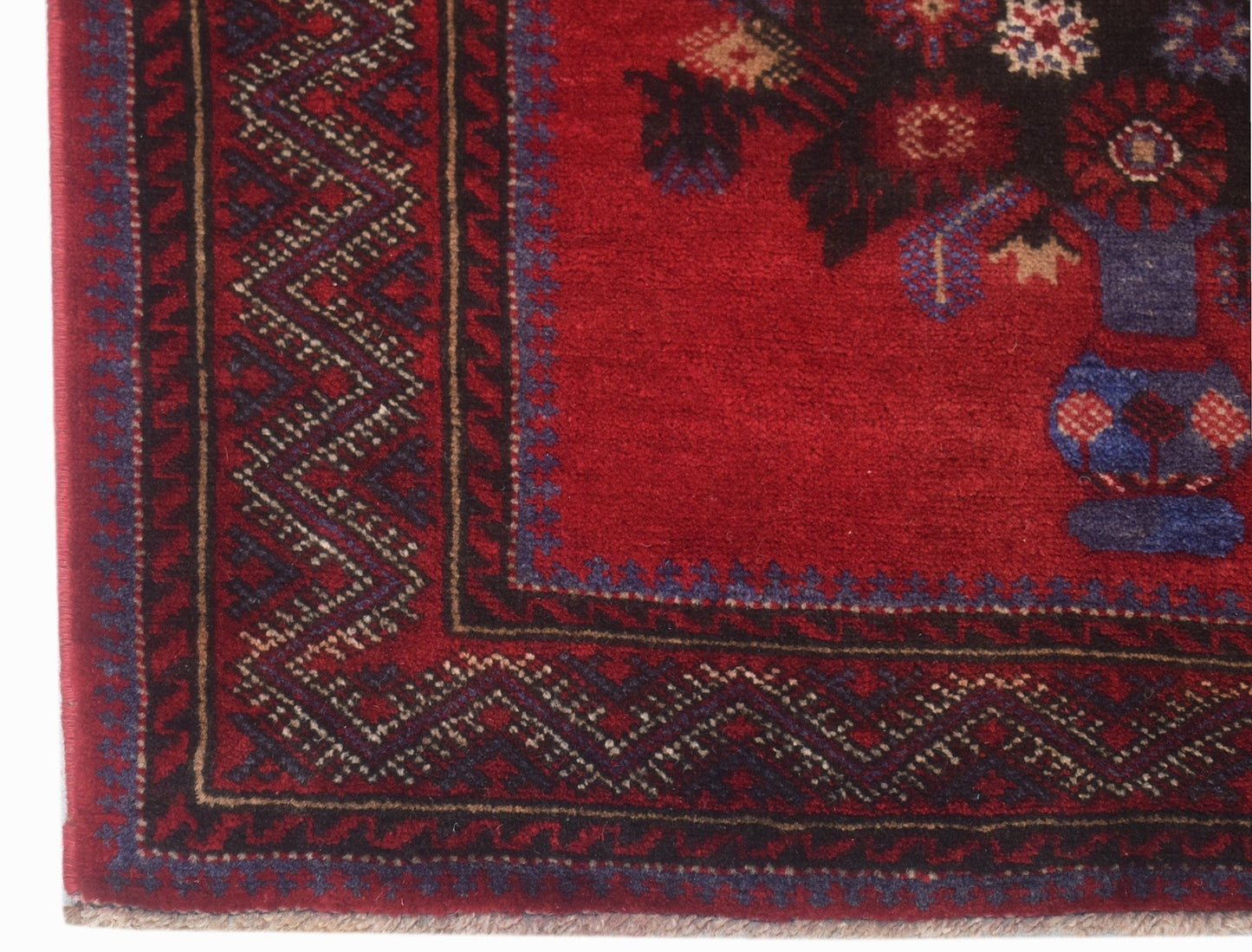 A close-up of a vintage Afghan Baluch rug featuring a red field with a floral vase motif.