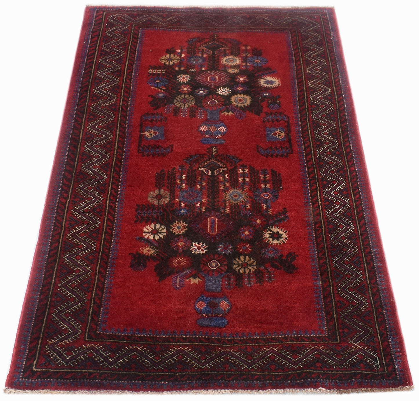 A vintage Afghan Baluch rug featuring two floral vase motifs on a deep red field.