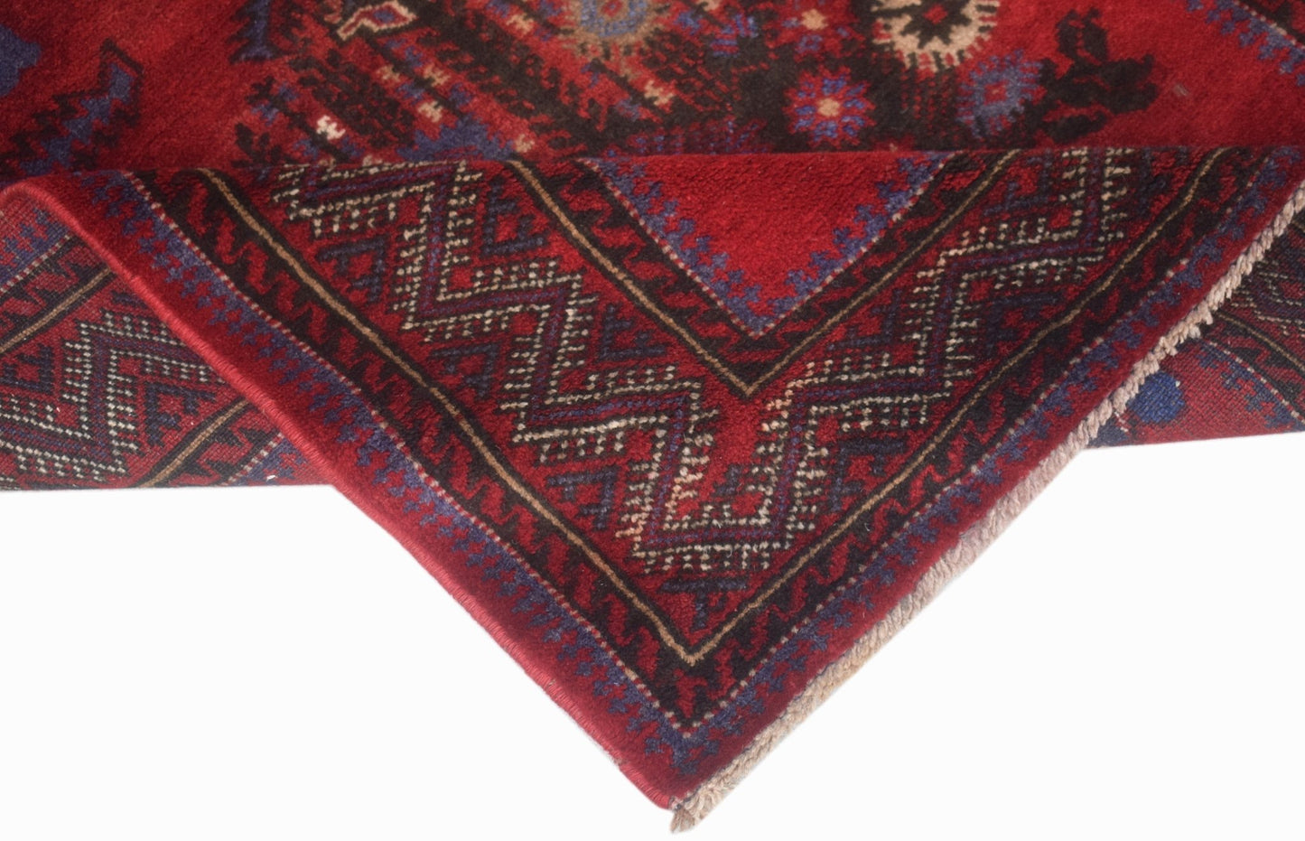A vintage Afghan Baluch rug featuring a red field with geometric patterns and a folded corner.