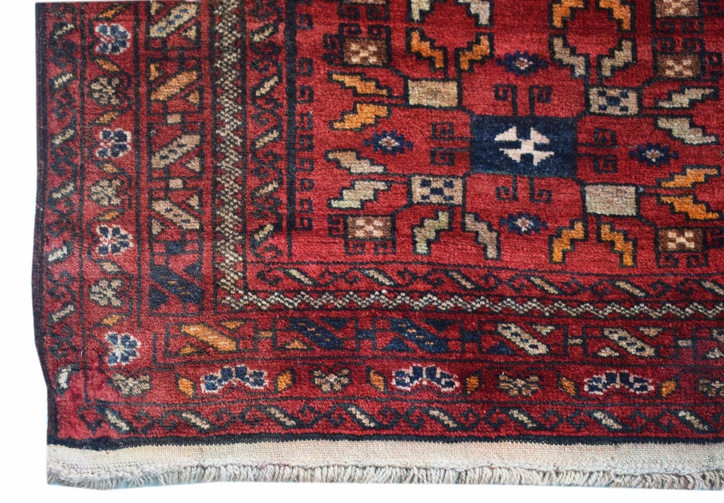 A handwoven vintage Afghan Baluch rug featuring geometric patterns in red, blue, and tan wool.