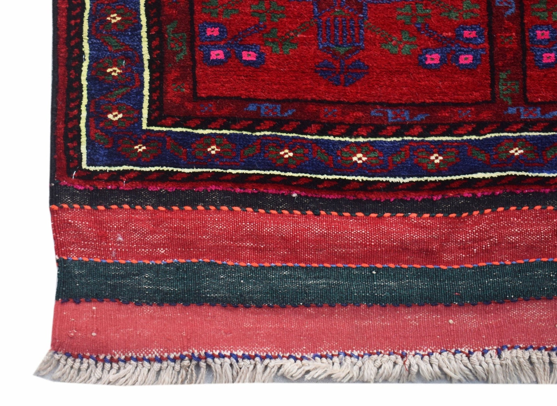 A close-up of a vintage Afghan Baluch rug featuring a red field, blue border, and fringed edge.