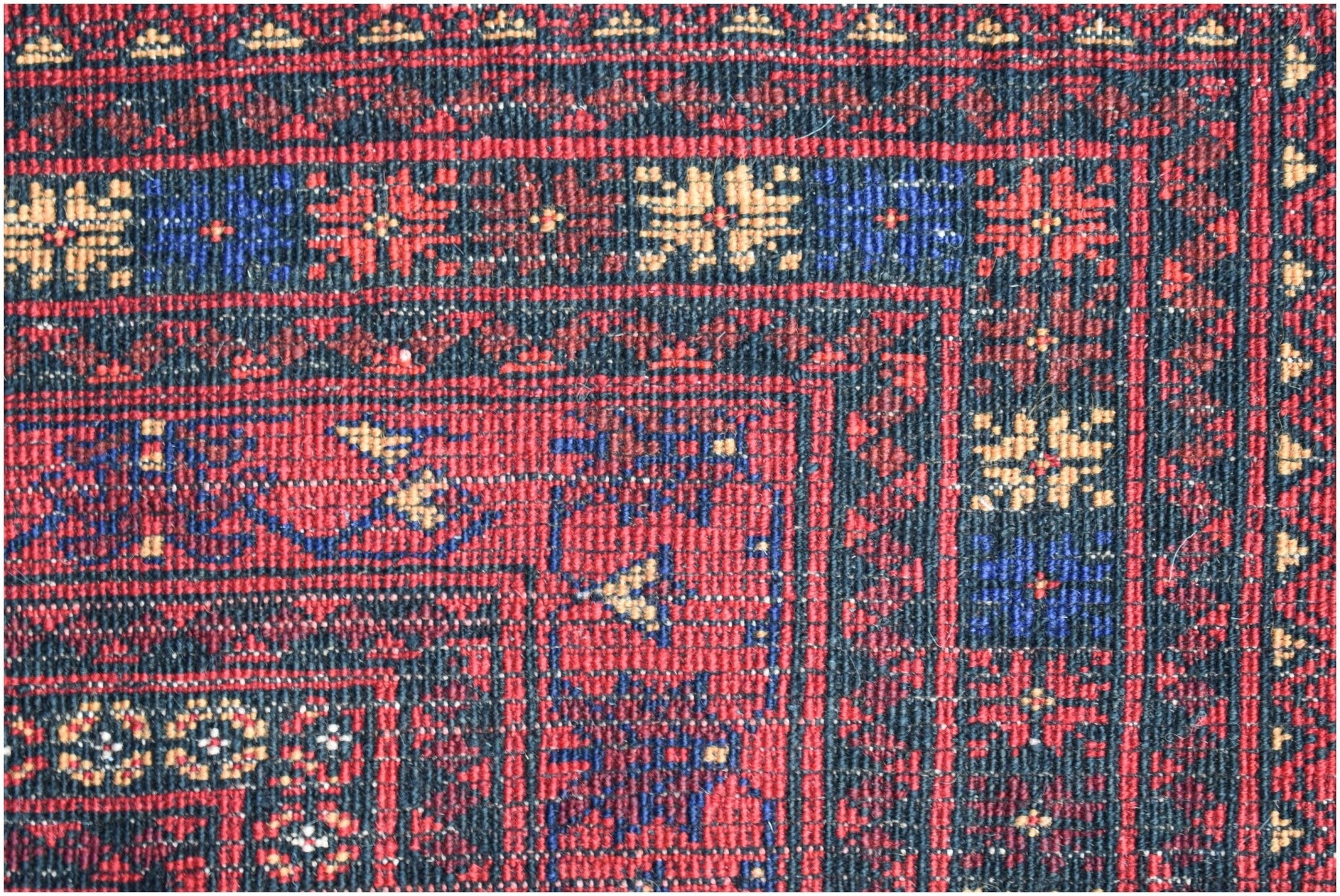 A close-up of a vintage Afghan Baluch rug featuring intricate geometric patterns in red and blue.