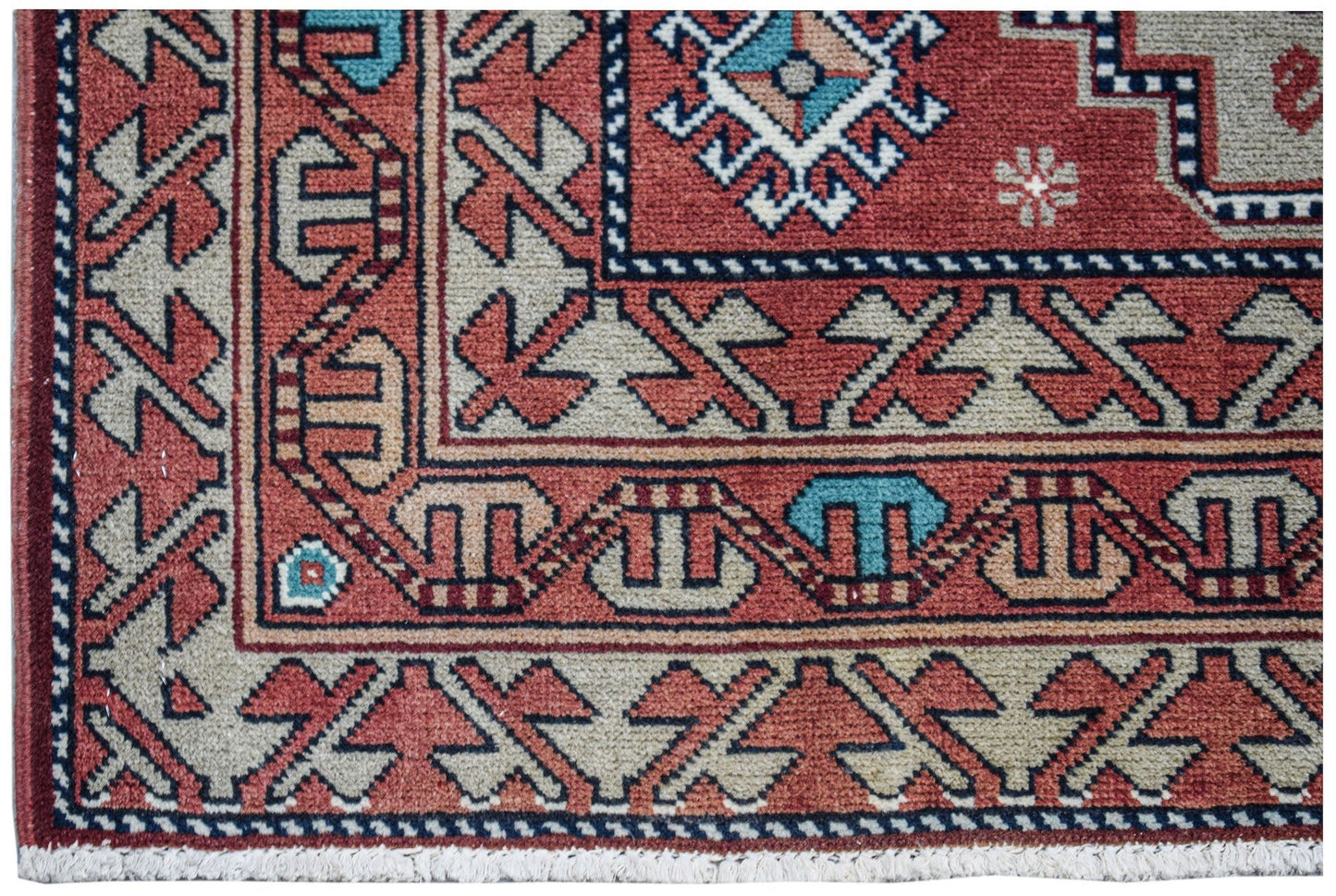 A vintage handwoven Caucasian wool rug featuring geometric patterns in red, blue, and beige.