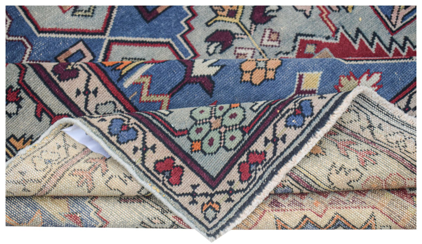 A vintage handwoven Caucasian wool rug featuring geometric patterns in blue, red, and beige.