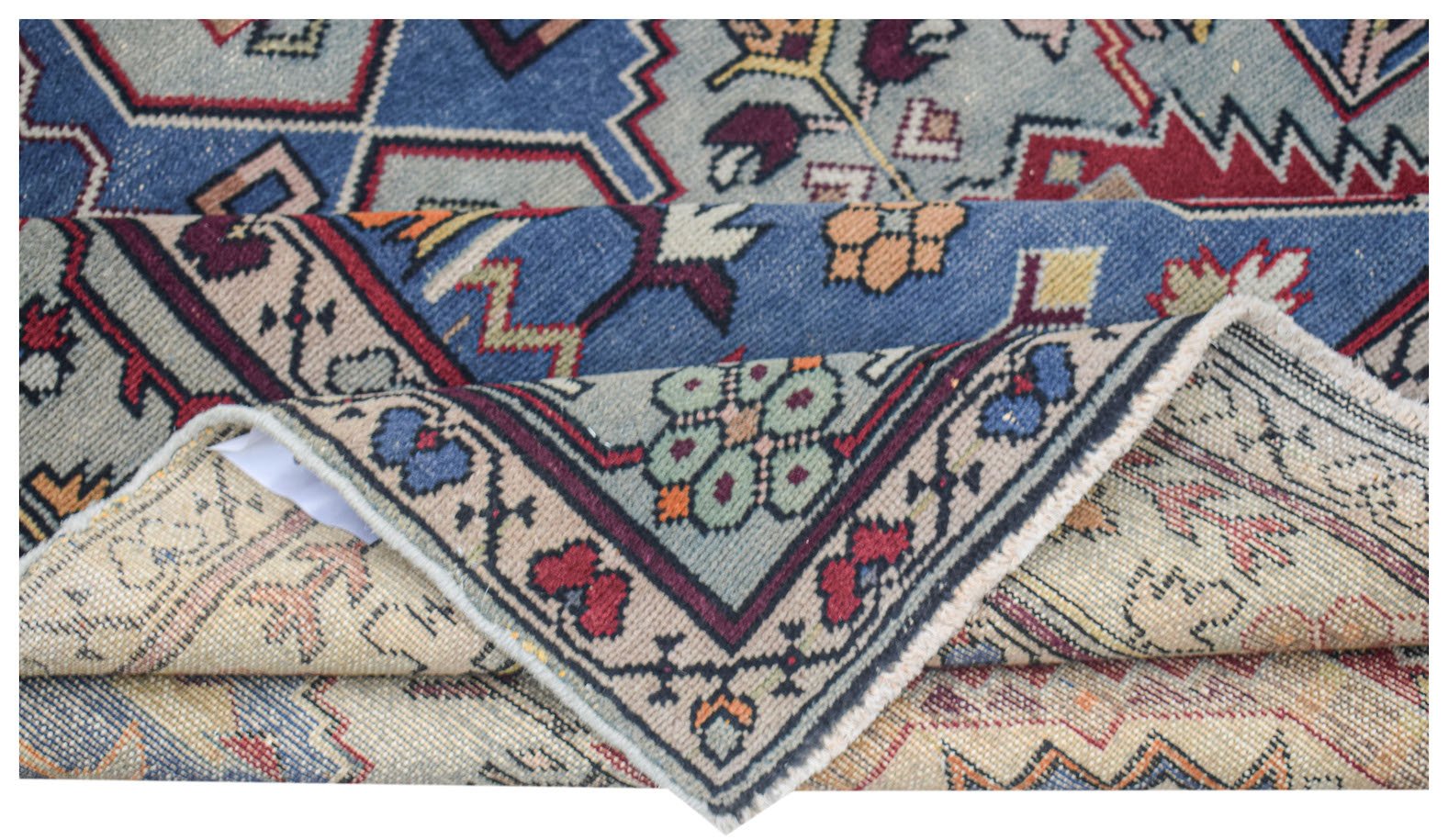 A vintage handwoven Caucasian wool rug featuring geometric patterns in blue, red, and beige.