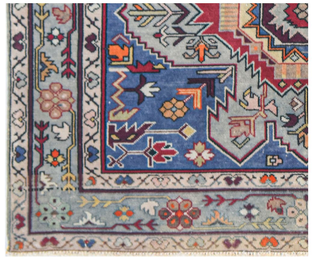 A vintage handwoven Caucasian rug featuring geometric floral patterns in blue, red, and cream.