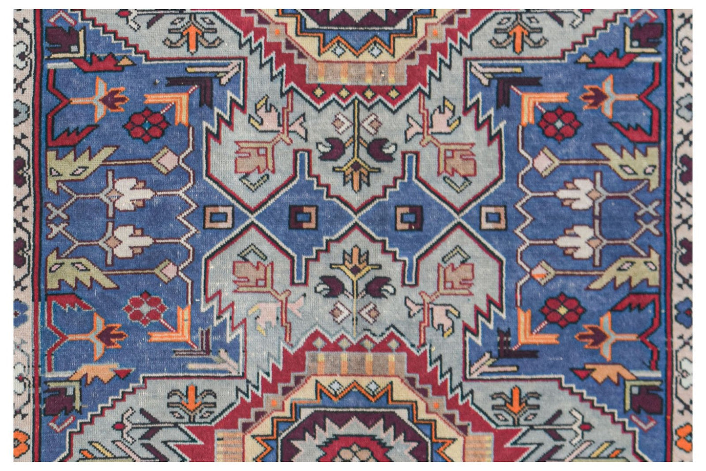 A vintage handwoven Caucasian rug featuring a geometric pattern in blue, red, and cream tones.