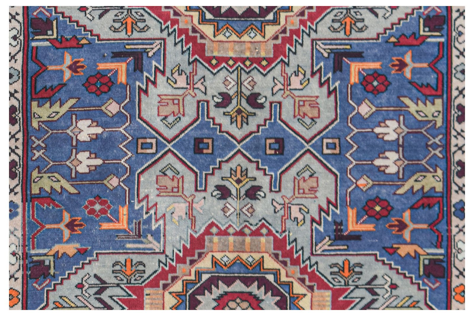 A vintage handwoven Caucasian rug featuring a geometric pattern in blue, red, and cream tones.