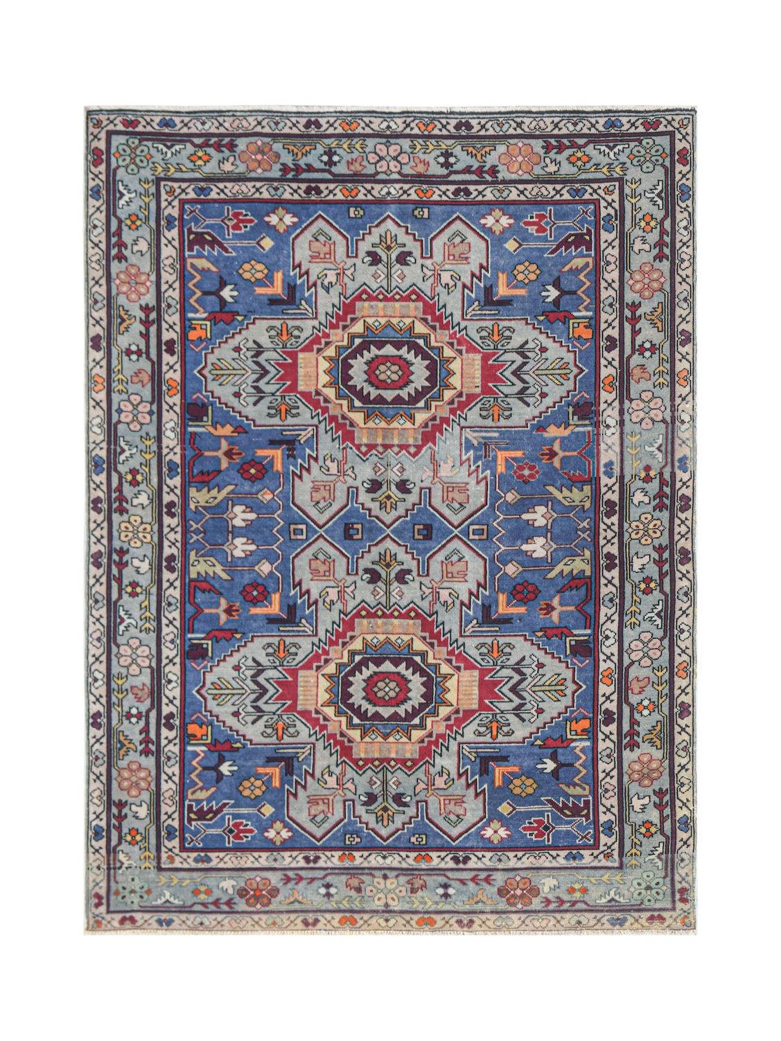 A vintage handwoven Caucasian rug featuring geometric medallions on a blue wool field.
