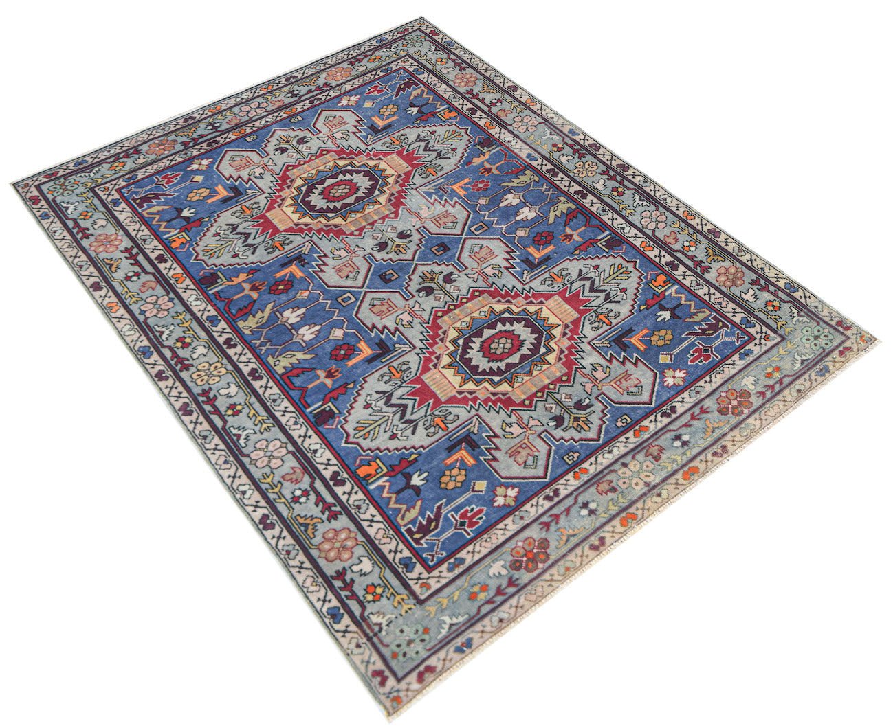 A vintage handwoven Caucasian rug featuring geometric patterns in blue, red, and cream tones.