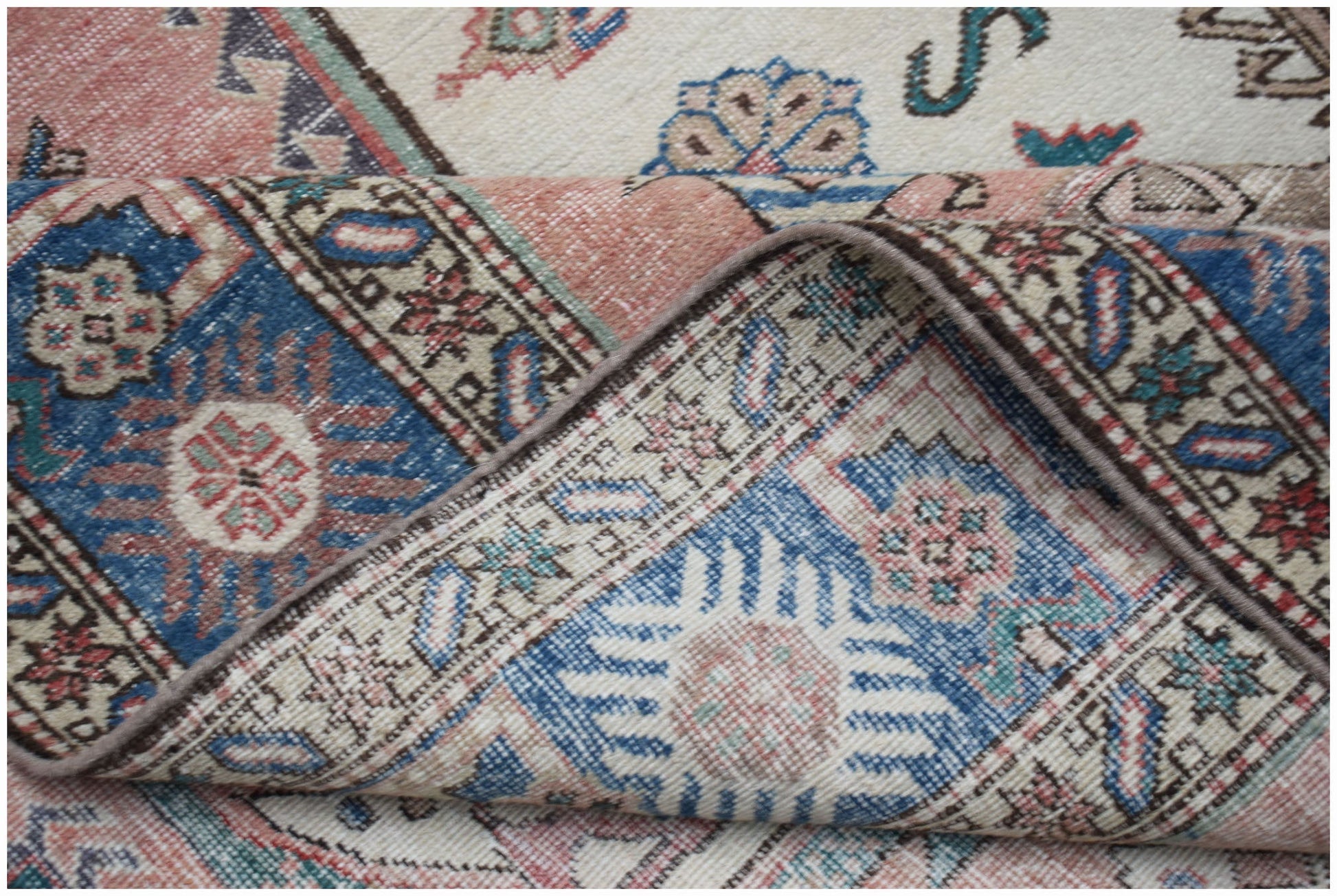 A vintage handmade wool rug featuring a traditional Caucasian pattern in blue, pink, and cream.