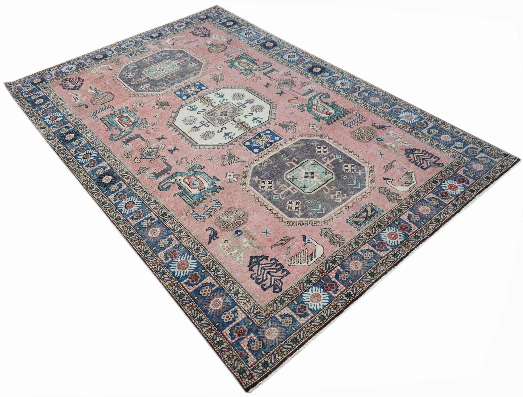 A vintage handmade Caucasian wool rug featuring a pink field with traditional geometric motifs.